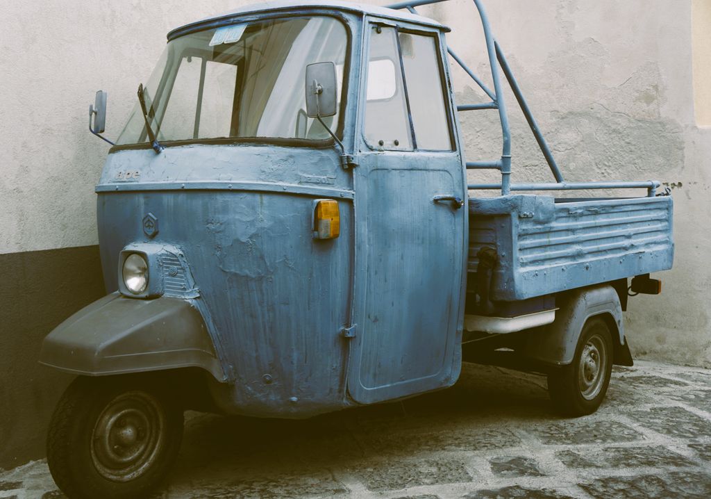 Rustikaler blauer Dreirad-Transporter vor einer Betonwand